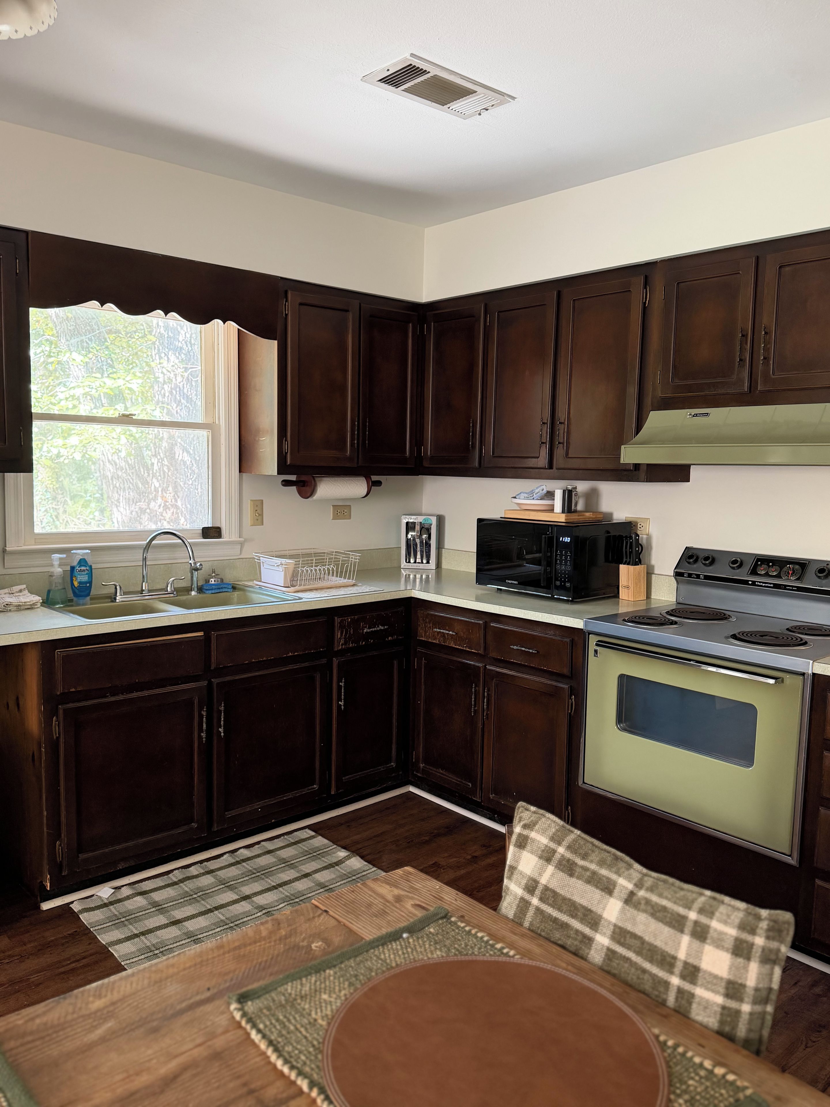 A kitchen with dark wooden cabinets, a stainless steel stove, and a window with a view of trees.