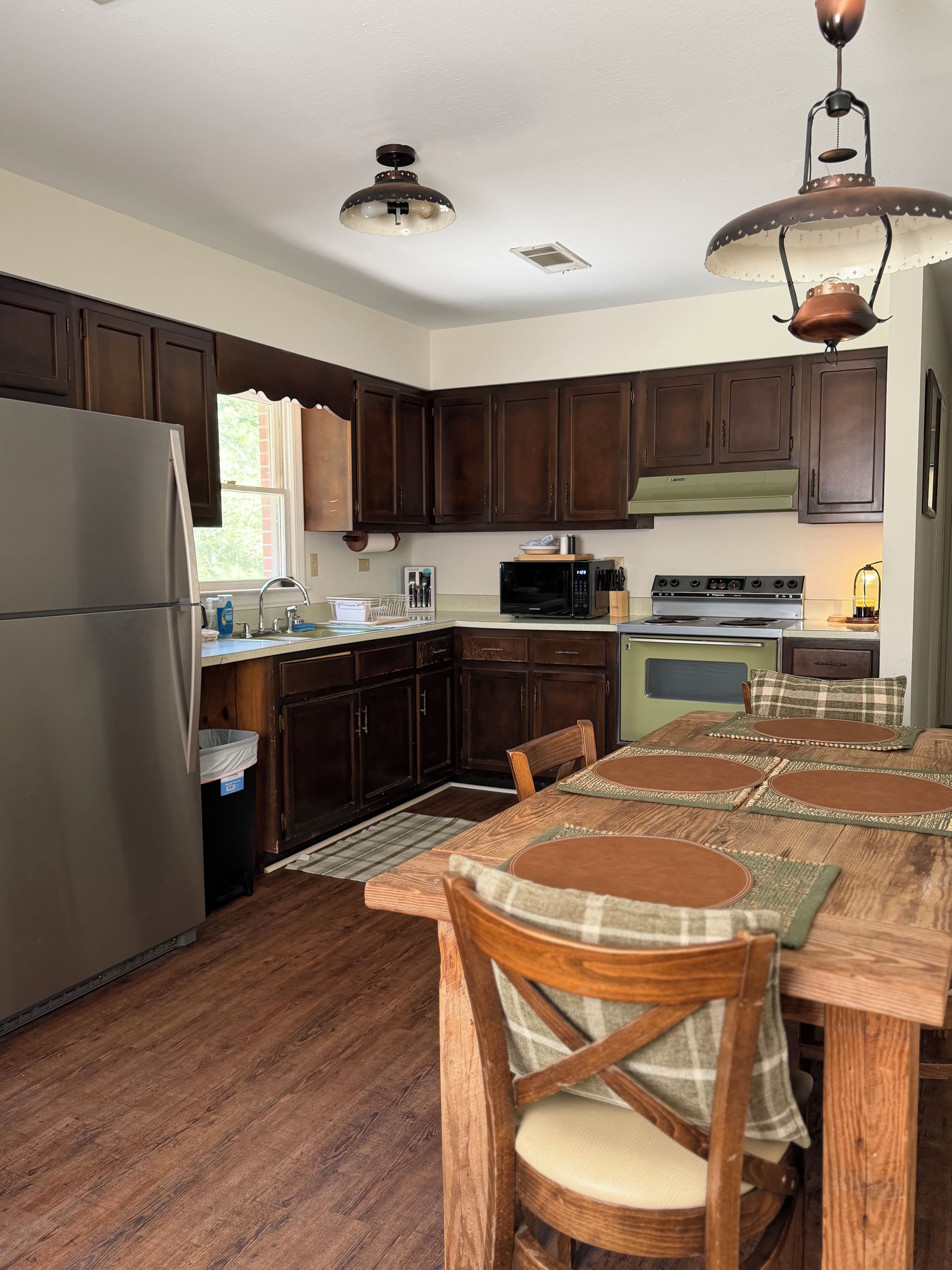 A kitchen with dark wooden cabinets, stainless steel appliances, and a dining area with a wooden table and chairs.