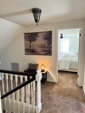 A staircase with white balusters, a hanging landscape painting, a lit table lamp, and a bedroom with a checkered bedspread. - Spacious  4-bedroom farmhouse located in East Dublin. (East Dublin)