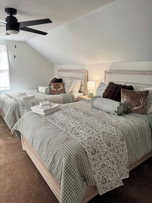 Quarto com duas camas, um ventilador de teto e uma mesa de cabeceira com abajur.