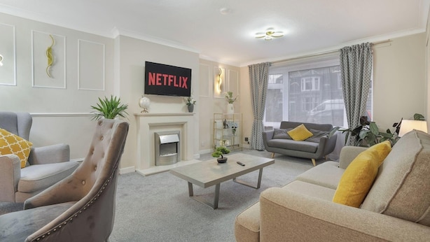 Een woonkamer met een open haard, een bank, een stoel, een salontafel en een aan de muur bevestigde televisie.