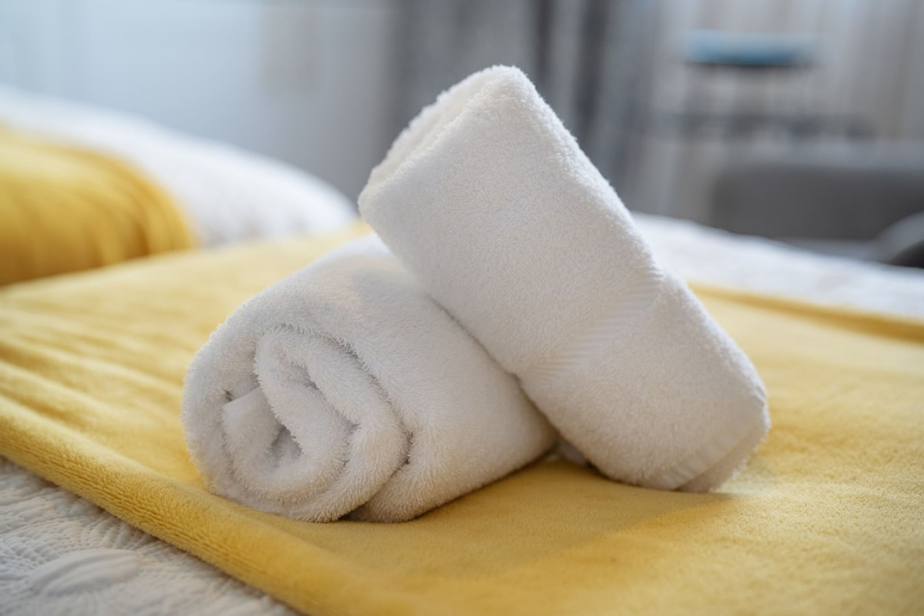 A neatly folded white towel on a yellow blanket, indicating a clean and well-maintained hotel room.