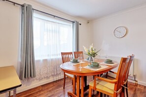 Ein Esszimmer mit einem runden Tisch, Stühlen, einer Blumenvase und einer Uhr an der Wand.
