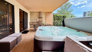 Ein moderner Außenbereich mit Whirlpool, Esstisch und Stühlen, einem großen Fenster und Blick zum Himmel.