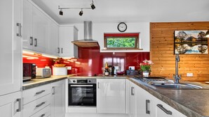 Una cucina moderna con mobili bianchi, uno schienale rosso, forno incassato, lavello e una finestra con vista sul verde.