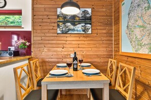 Una habitación con paneles de madera, una mesa de comedor lista para dos personas, un mapa en la pared y una ventana con follaje en el exterior.