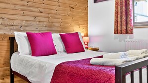 Una camera d'albergo con una parete in legno, un letto con biancheria da letto bianca e rosa, una coperta rossa e una finestra con tende.