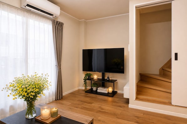 A living room with a flat-screen TV, a wooden staircase, and a vase of yellow flowers.