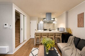 A modern kitchen with a central island, a dining area with chairs, a sofa, and a coffee table with flowers.
