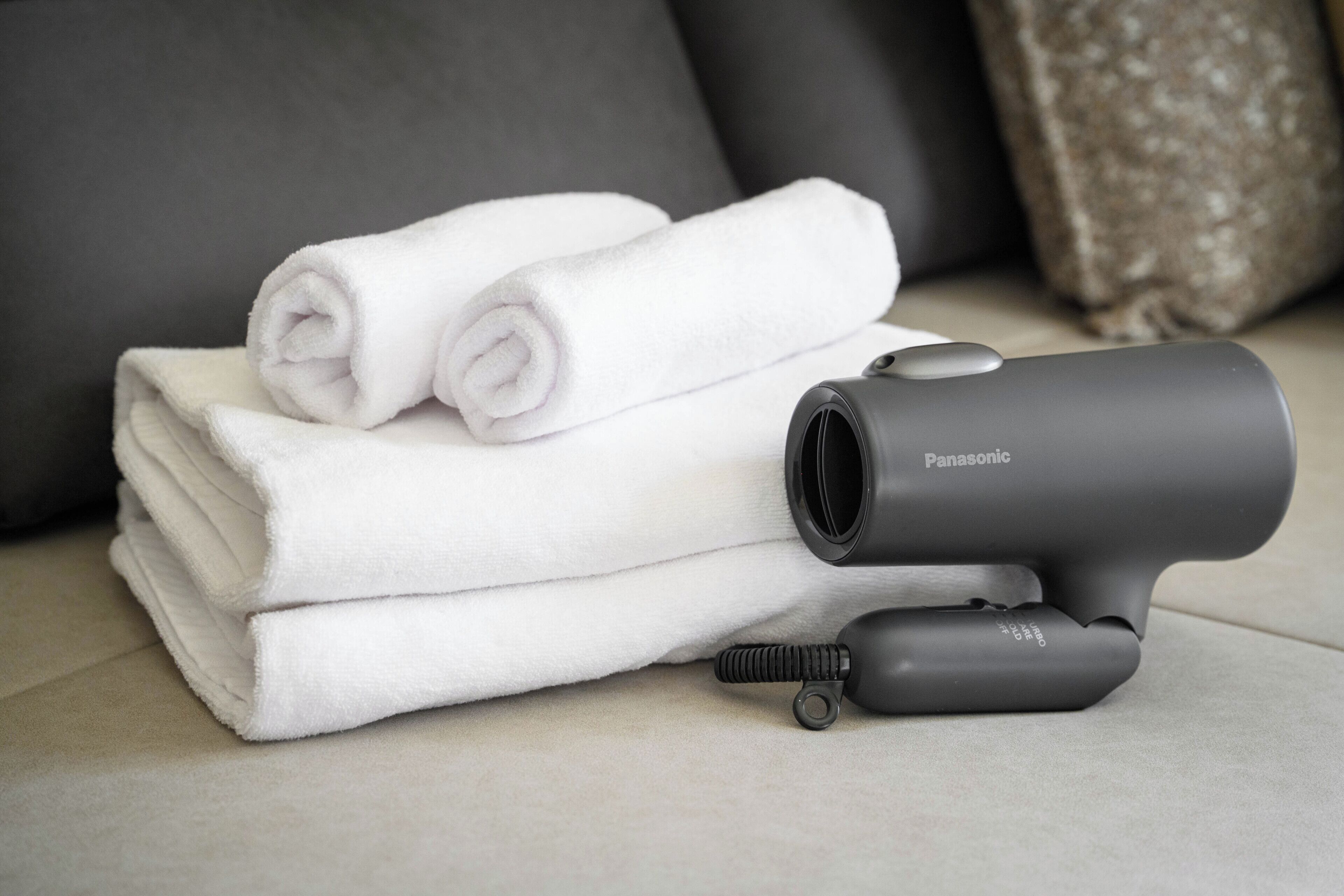 A Panasonic hair dryer on a light-colored surface with neatly folded white towels.