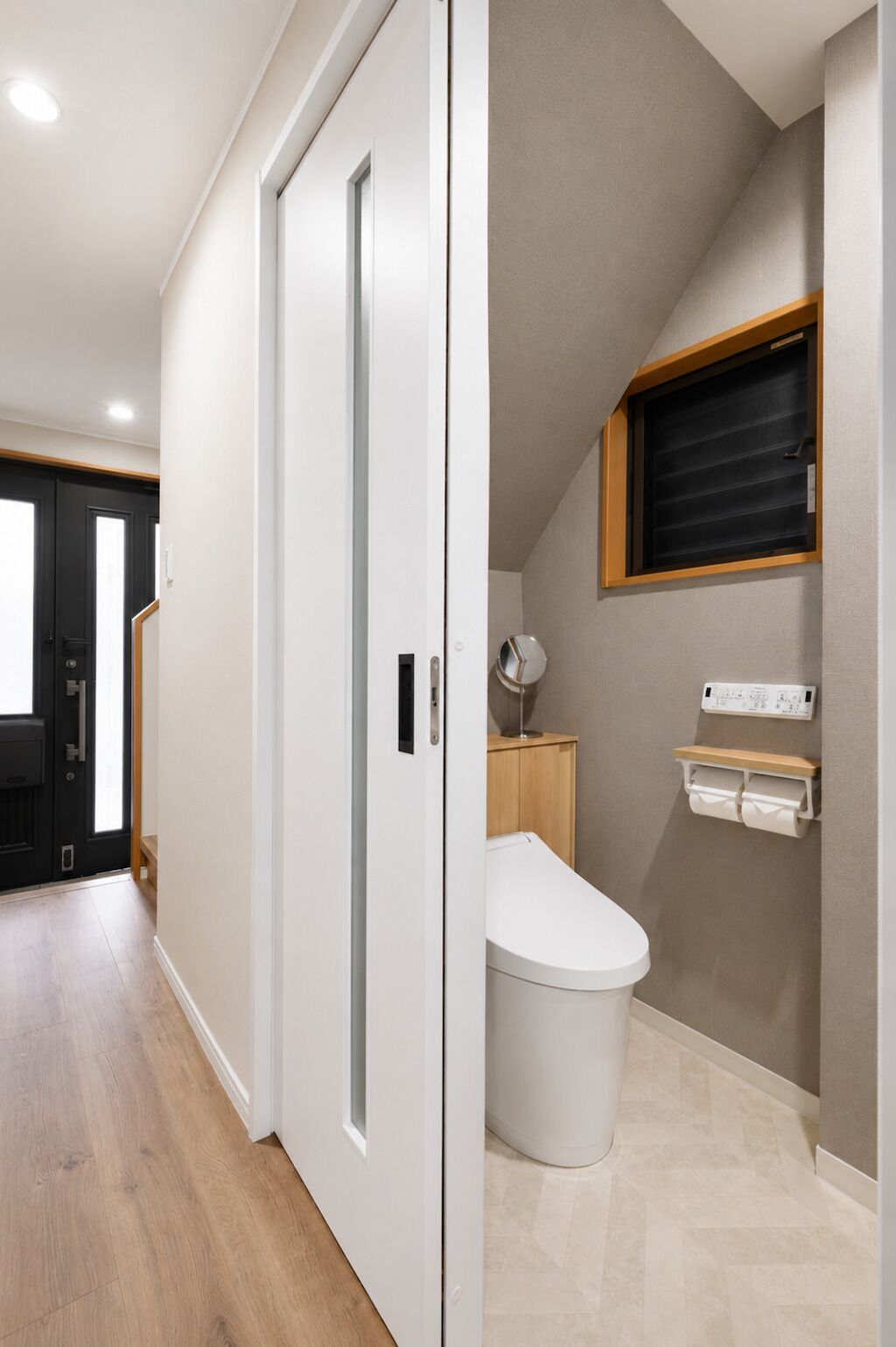 A modern bathroom with a toilet, a small window, and a wall-mounted electrical outlet.