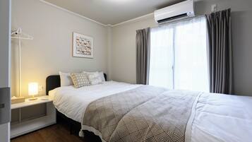 A hotel room with a bed, bedside table, lamp, air conditioning unit, and a window with curtains.