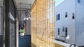 Un balcó estret amb una barrera de xarxa groga, una planta penjant i vista d'un edifici blanc.
