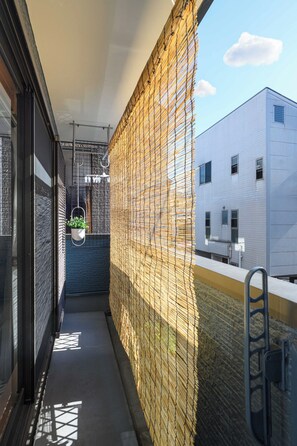 A narrow balcony with a yellow net barrier, a hanging plant, and a view of a white building. - Metro House Tsuruhashi - Self Check-In (Osaka, Ikuno Ward, Tsuruhashi)