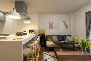 A modern living space with a kitchen area, a sofa, a coffee table, and a dining set. - Metro House Tsuruhashi - Self Check-In (Osaka, Ikuno Ward, Tsuruhashi)