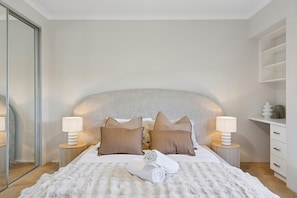 A bedroom with a large bed, two bedside lamps, a mirror, and a white wardrobe.