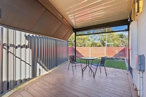 An outdoor patio with a covered area, a table with chairs, and a view of a backyard with a wooden fence.
