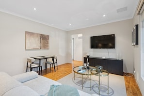 A modern living room with a sofa, a dining table, and a TV mounted on the wall.