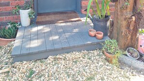Una puerta azul con felpudo, plantas en macetas y un árbol con enredaderas.