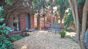 Un patio trasero con una casa de ladrillo, un banco de madera y una planta en maceta.