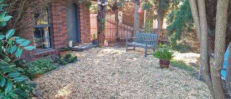 Un patio trasero con una casa de ladrillo, un banco de madera y una planta en maceta.
