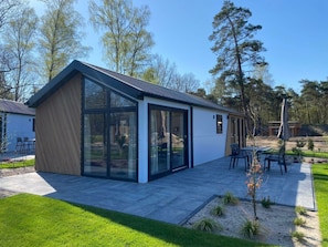 Ein modernes Haus mit einem großen Panoramafenster, einer Terrasse mit Gartenmöbeln und einem gepflegten Rasen.