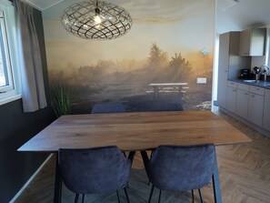 Eine moderne Küche mit einem Holztisch und Stühlen, einer Pendelleuchte und einem Wandbild eines Waldmotivs.
