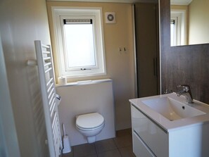 Ein Badezimmer mit Toilette, Fenster, Heizkörper, Waschbecken und Spiegel.