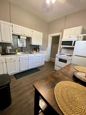 A modern kitchen with white cabinets, a wooden dining table, and a microwave. - Prime Downtown Owensboro Stay • 2BR Steps to Riverfront & Brescia (Owensboro)