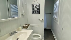 Un baño con lavamanos, espejo y retrete blancos. Hay un cartel en la pared que dice 'LIVE LOVE LAUGH'.