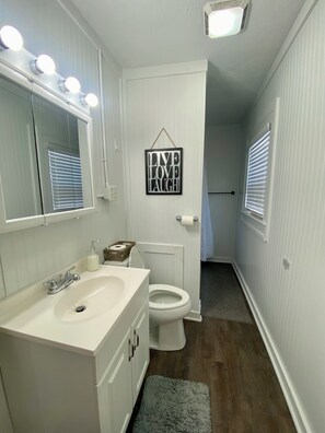 A bathroom with a white sink, mirror, and toilet. There is a sign on the wall that says 'LIVE LOVE LAUGH'. - Prime Downtown Owensboro Stay • 2BR Steps to Riverfront & Brescia (Owensboro)