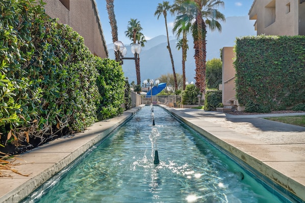 A swimming pool with clear water, surrounded by greenery and palm trees. - Charming Downtown Palm Springs Getaway 1 Bedroom Condo (Palm Springs)