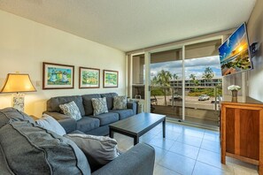 A living room with a sofa, coffee table, and artwork on the wall. - Maui Banyan H406 1 Bedroom Condo (Kihei)