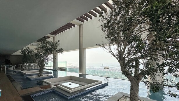An infinity pool with a view of the city, a tree planter, and a seating area. - Chic 2BR in Paramount Midtown Infinity Pool Access (Dubai)