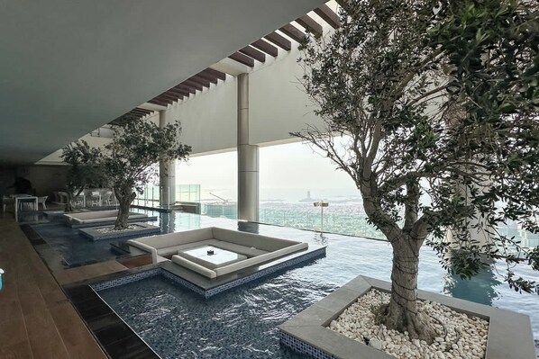 Ein Pool im Infinity-Stil mit Blick auf die Stadt, ein Baumbeet und eine Sitzgelegenheit.
