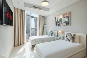 Ein Hotelzimmer mit zwei Betten, einem Fernseher, einem Gemälde und Blick auf die Stadt.