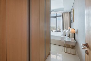 Ein Hotelzimmer mit Bett, Nachttisch, Lampe und Blick auf die Stadt durch große Fenster.