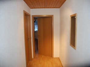 Ein schmaler Korridor mit Holzboden, weißen Wänden und Holzbalkendecke.
