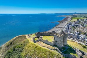 Vista aérea de un pueblo costero con ruinas históricas, una playa y zonas residenciales.