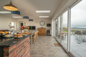 A spacious kitchen with a large island, a dining area with a view, and a cozy seating area. - Large Holiday Cottage With Hot Tub Near Abersoch | Neigwl (Pwllheli)