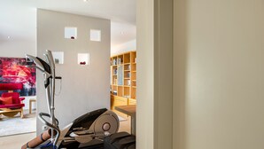 A home gym with a stationary bike, a red chair, and a bookshelf.
