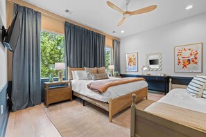 Ein Schlafzimmer mit Bett, Nachttischen, einer Kommode, einem Deckenventilator und Kunstwerken an den Wänden.
