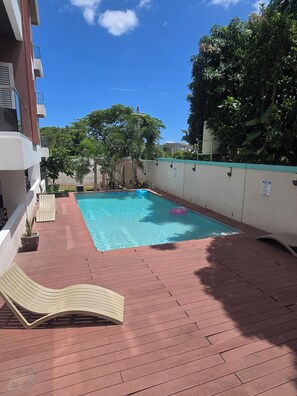 Una piscina con sillones de descanso, una terraza de madera y un edificio con fachada blanca.