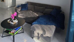 Ein Wohnzimmer mit einer Couch, einem Couchtisch mit Blumen und einem Gemälde einer Strandansicht.