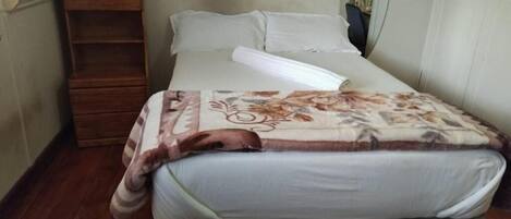 A single bed with a patterned blanket, a wooden shelf, and a painting on the wall.