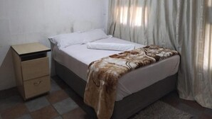 Un dormitorio con cama, mesita de noche y ventana con cortinas.