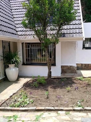 Una casa con techo de tejas, un pequeño jardín con un árbol y una planta en maceta.