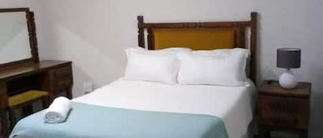 A bedroom with a bed, a nightstand, a lamp, a painting, and a wooden headboard.