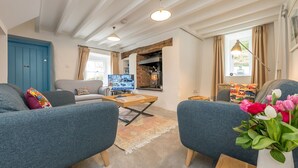 Een woonkamer met een blauwe bank, een salontafel en een televisie. Er is een open haard en een raam met gordijnen.