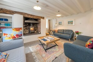 A cozy living room with a fireplace, a sofa, a coffee table, and a television. - Beautiful Cosy Cottage Overlooking Beaumaris Bay | Rallt-Goch-Bach (Beaumaris)
